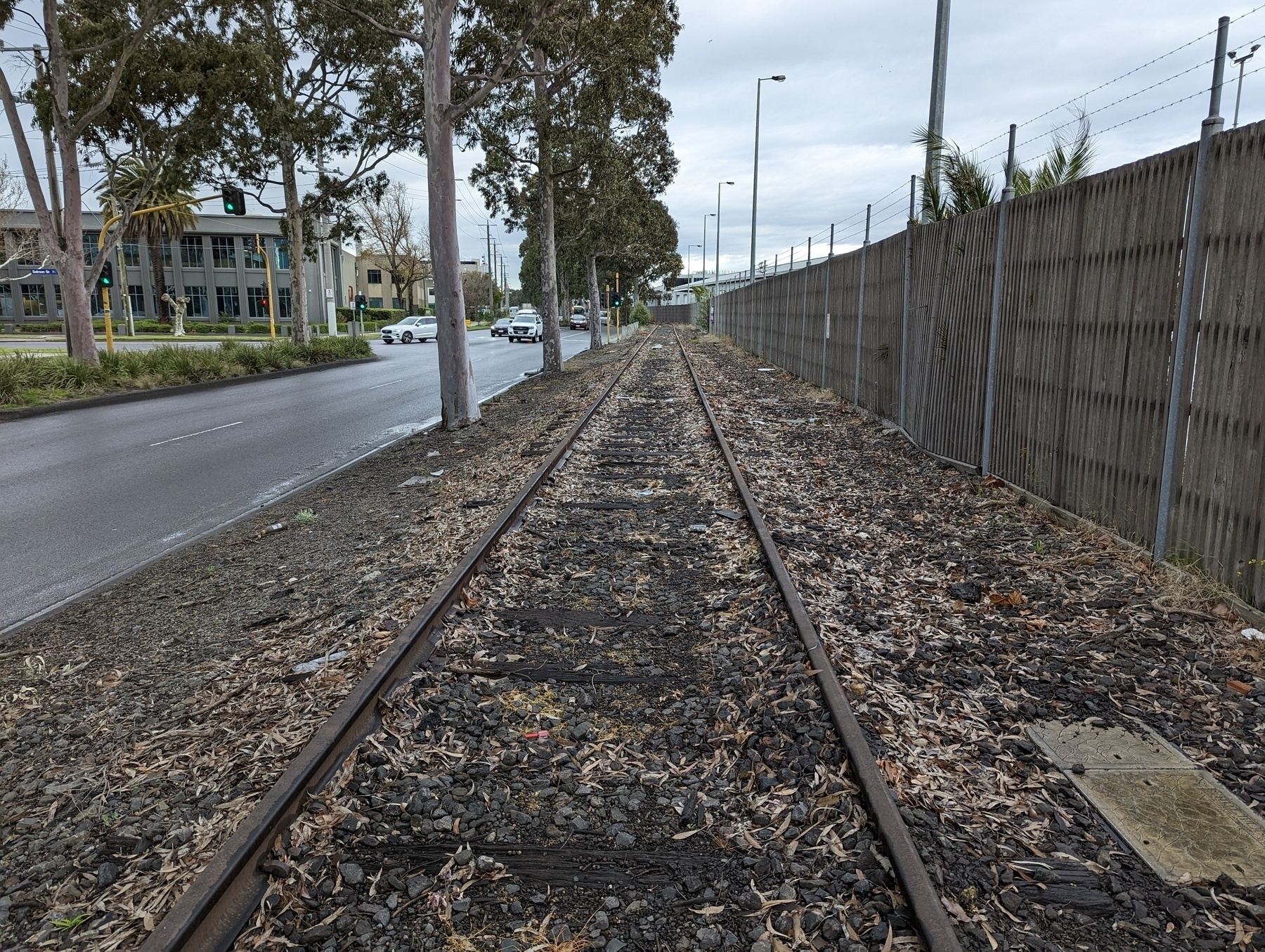 Railway tracks with a road on the left and the Melbourne Port fence on the right.