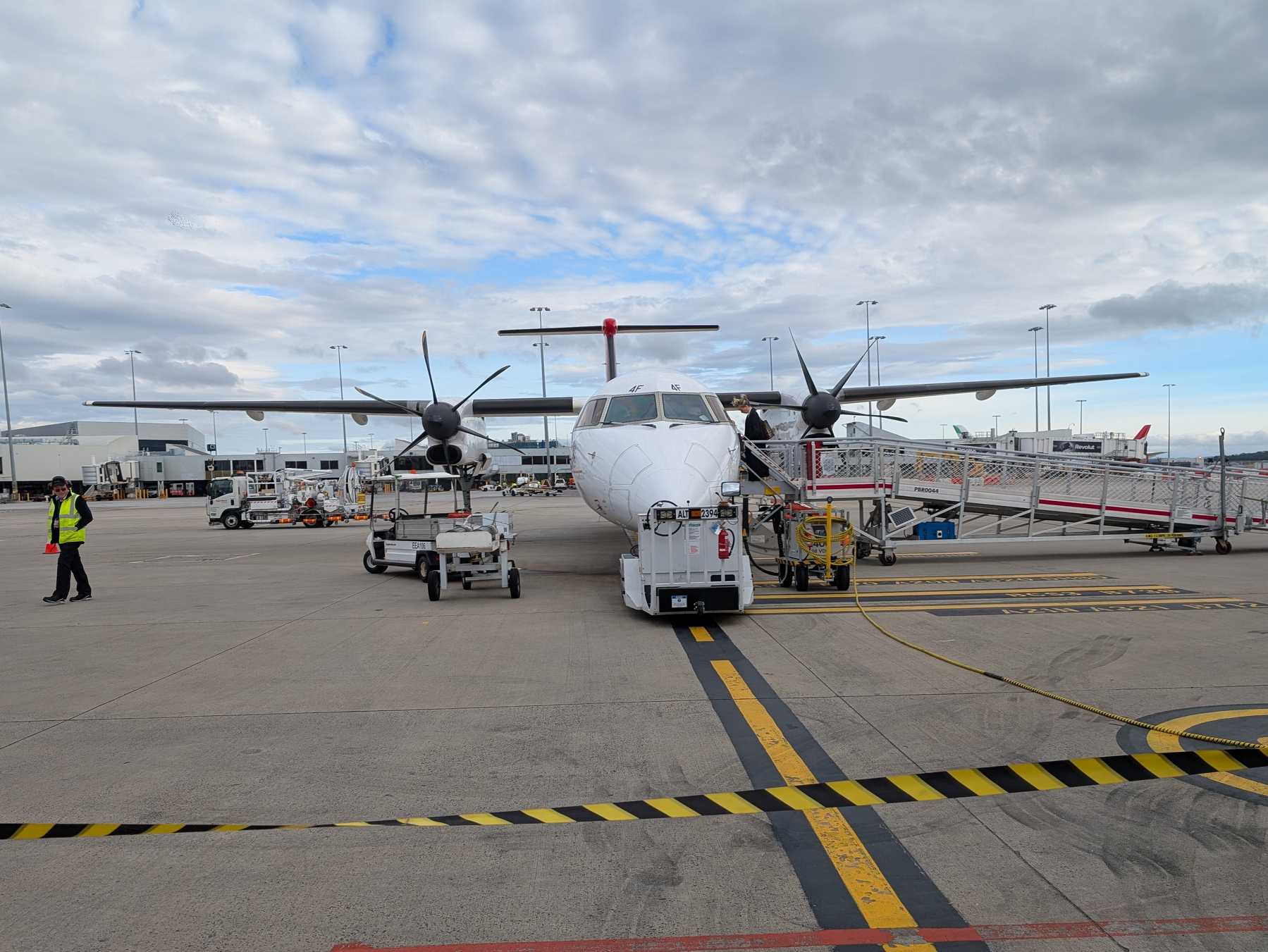 Auto-generated description: A turboprop airplane is parked on an airport tarmac with ground support equipment and personnel nearby.